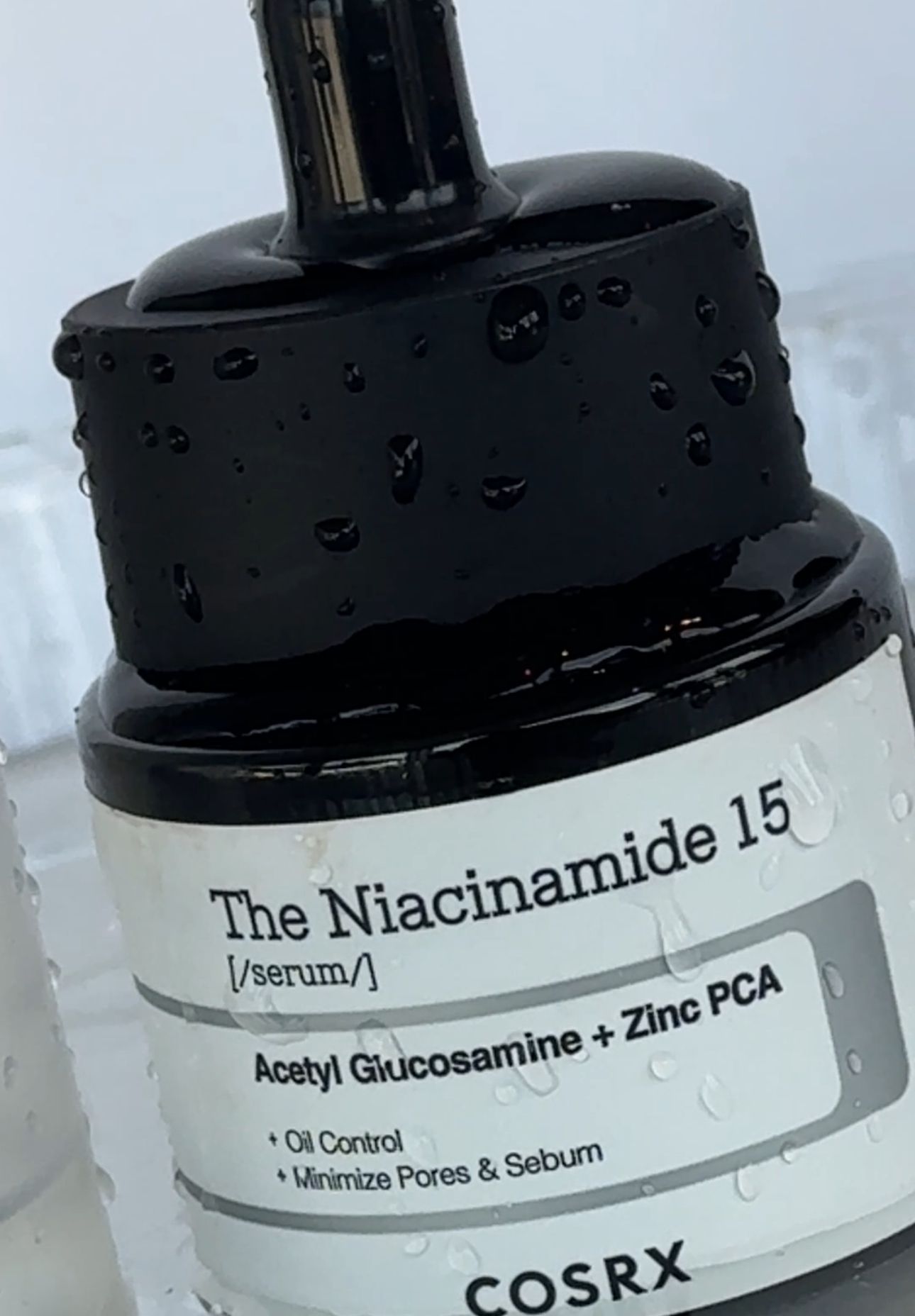 Produktfoto av COSRX The Niacinamide 15 serum, avbildet med vanndråper for en frisk og ren look. Nærbilde som fremhever tekstur og fukt, ideelt for skjønnhets- og hudpleieinnhold.